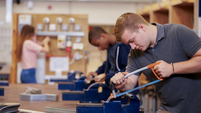 Teenager cutting with a saw in class