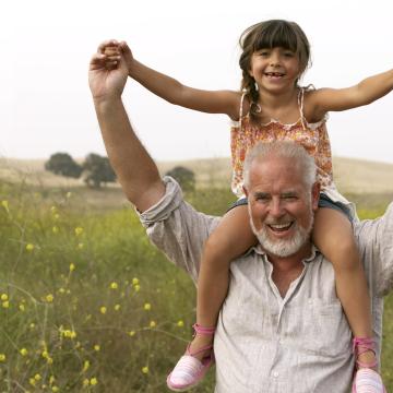 A man is carrying a little girl on his shoulders in a field.