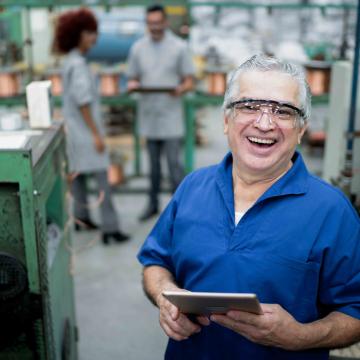 White man in blue shirt holding a tablet while working in a factory